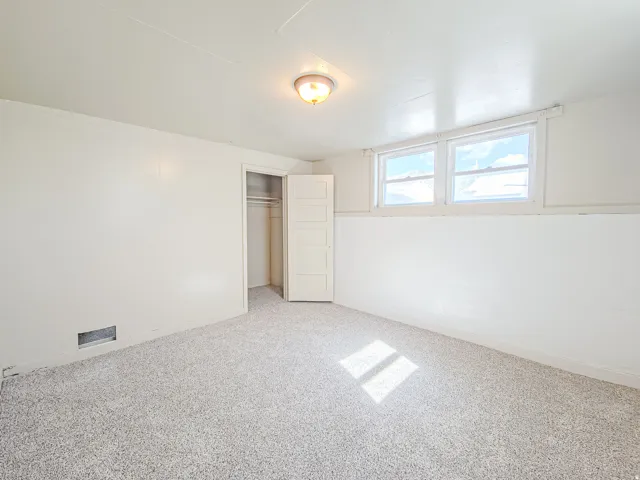 Light-colored carpeting, two windows, wall-mounted light fixture, and an open closet