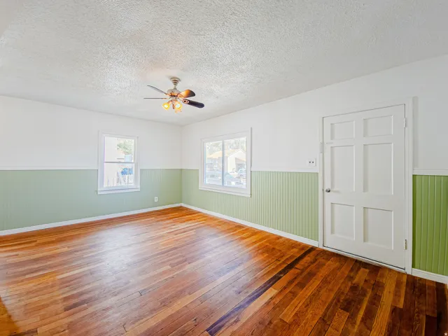 Hardwood flooring, painted beadboard wainscoting, white trim, multiple windows, and a ceiling fan with integrated lighting