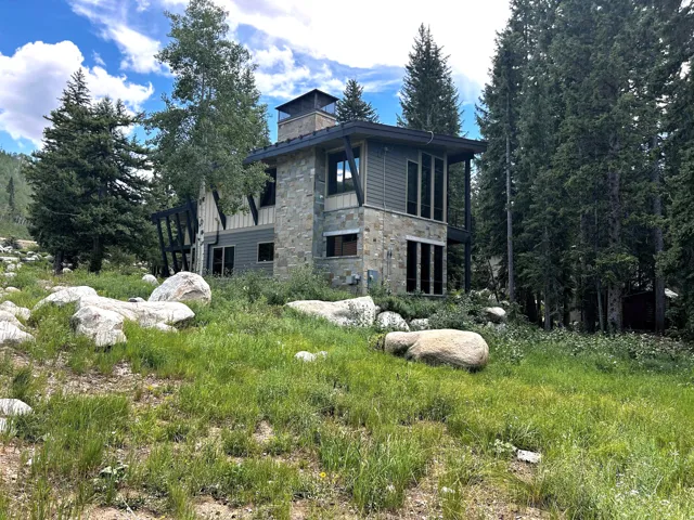 Stone and siding exterior with expansive windows, a prominent stone chimney, and a surrounding natural landscape with mature trees