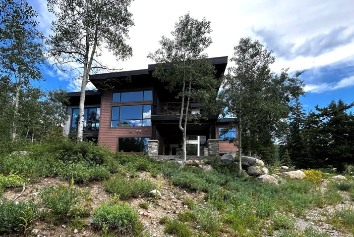 Modern architecture with expansive windows, wood-finish siding, stone accents, and a tiered landscape with mature trees
