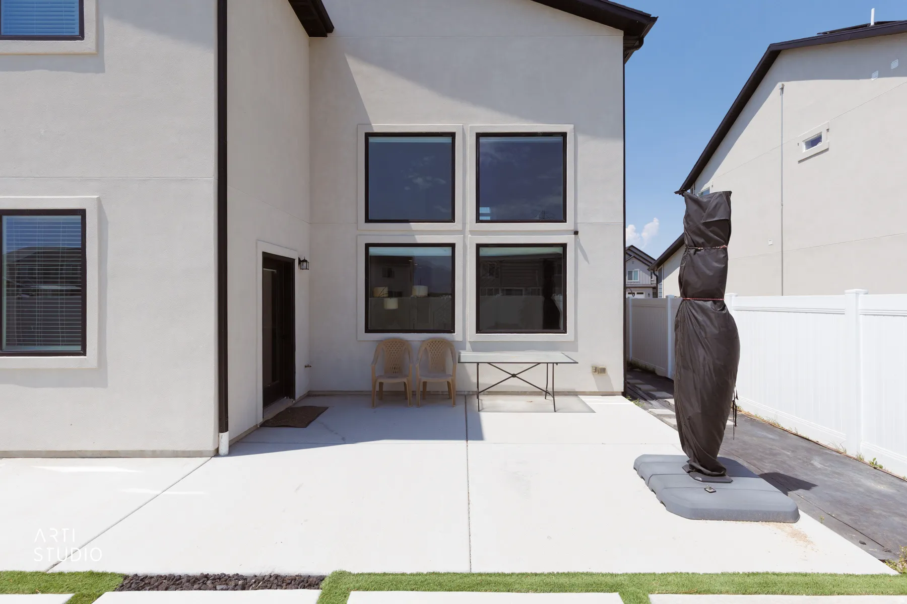 Stucco exterior with black-framed windows, a white privacy fence, concrete patio, and integrated artificial turf accents