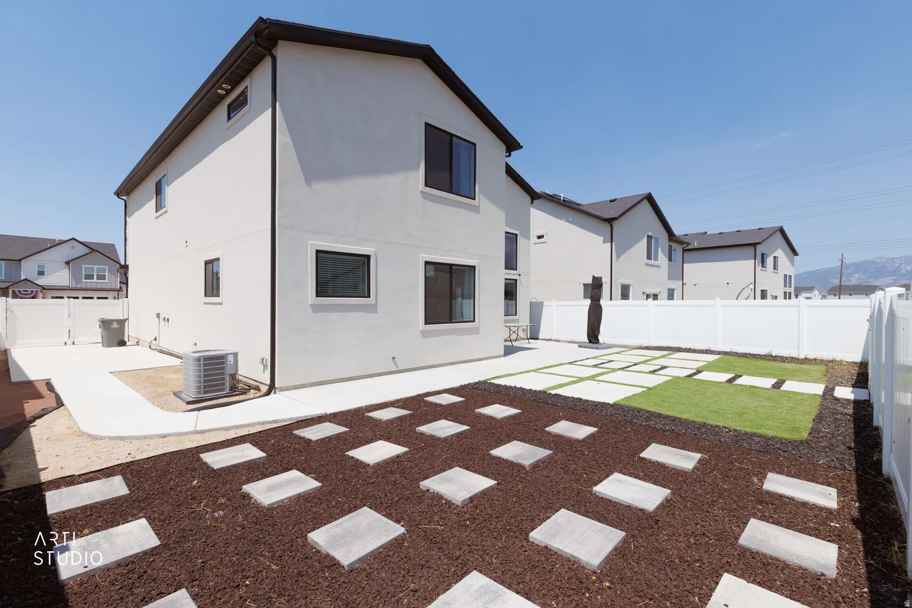 Expansive backyard featuring a white vinyl fence, concrete patio, stepping stones, and a manicured lawn