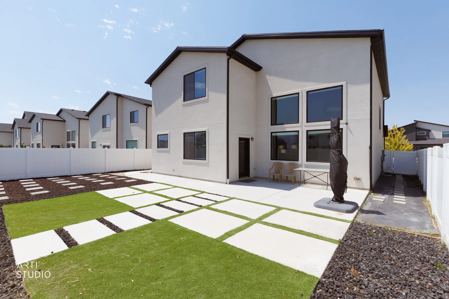 Rear exterior featuring a large concrete patio, expansive windows, artificial turf, and decorative hardscaping