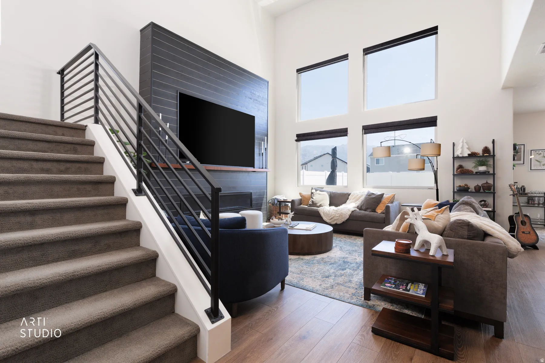 Soaring vaulted ceiling, wood-finish flooring, two-story window array, fireplace with a tile surround, and an open-tread staircase with metal railings