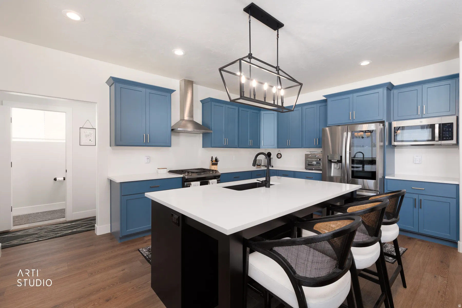 Kitchen featuring wood-finish flooring, blue cabinetry, a white countertop, stainless steel appliances, and a central island with a sink