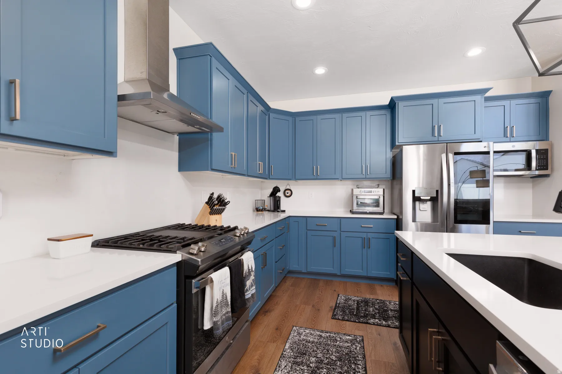 Kitchen with blue cabinetry, white countertops, stainless steel appliances, and wood-finish flooring