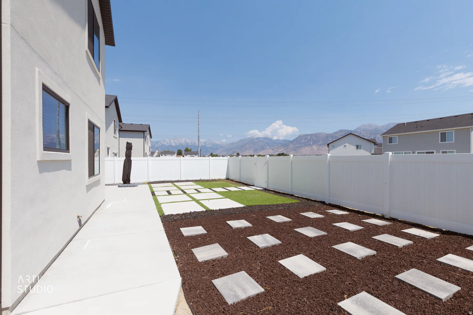 Private backyard featuring a white vinyl fence, stepping stones, and a grass area