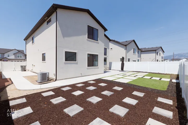Expansive backyard featuring a white vinyl fence, concrete patio, stepping stones, and a manicured lawn
