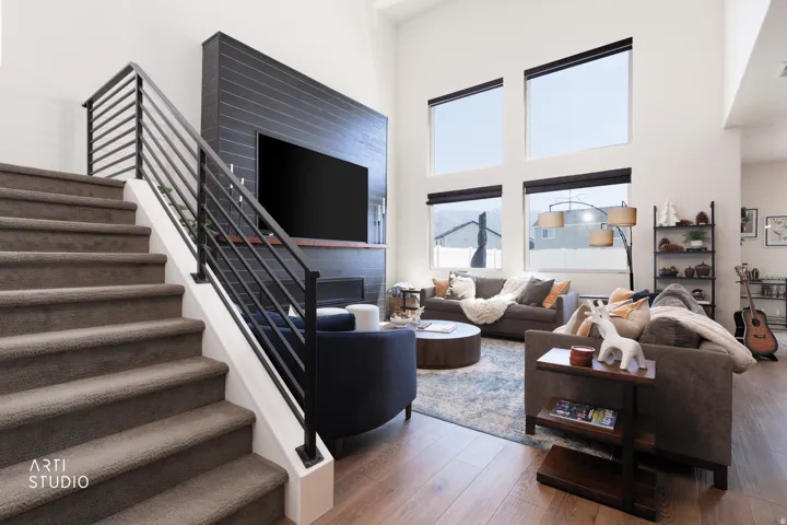 Soaring vaulted ceiling, wood-finish flooring, two-story window array, fireplace with a tile surround, and an open-tread staircase with metal railings