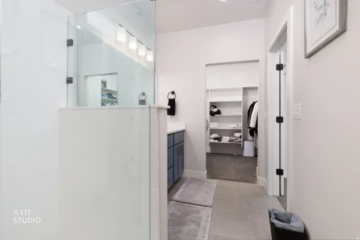 Walk-in shower with glass enclosure, single vanity with integrated sink, recessed lighting, and an adjacent walk-in closet with built-in shelving