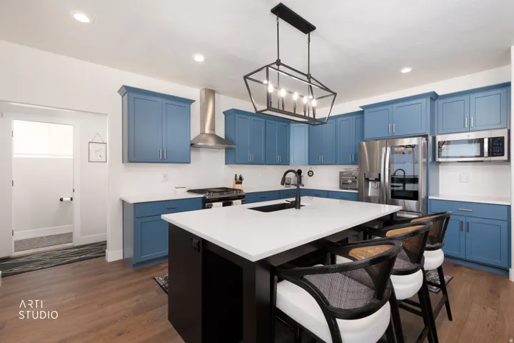 Kitchen featuring wood-finish flooring, blue cabinetry, a white countertop, stainless steel appliances, and a central island with a sink