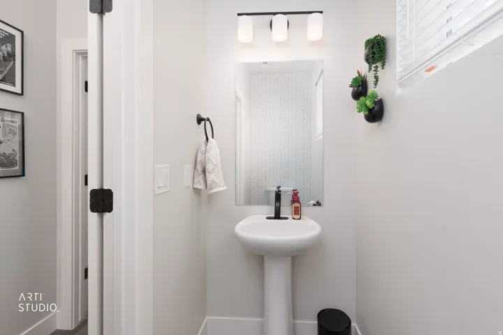 Pedestal sink with a matte black faucet, wall-mounted mirror, and a three-light vanity fixture
