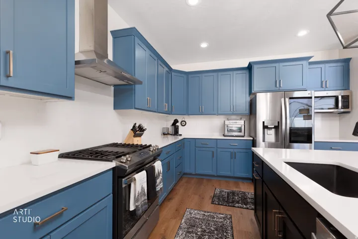 Kitchen with blue cabinetry, white countertops, stainless steel appliances, and wood-finish flooring