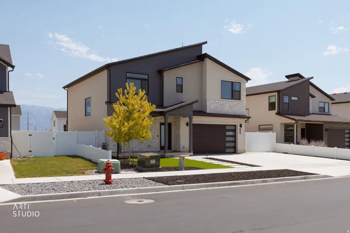 Modern exterior with stucco and dark gray siding accents, attached garage with horizontal paneling, concrete driveway, and front yard landscaping