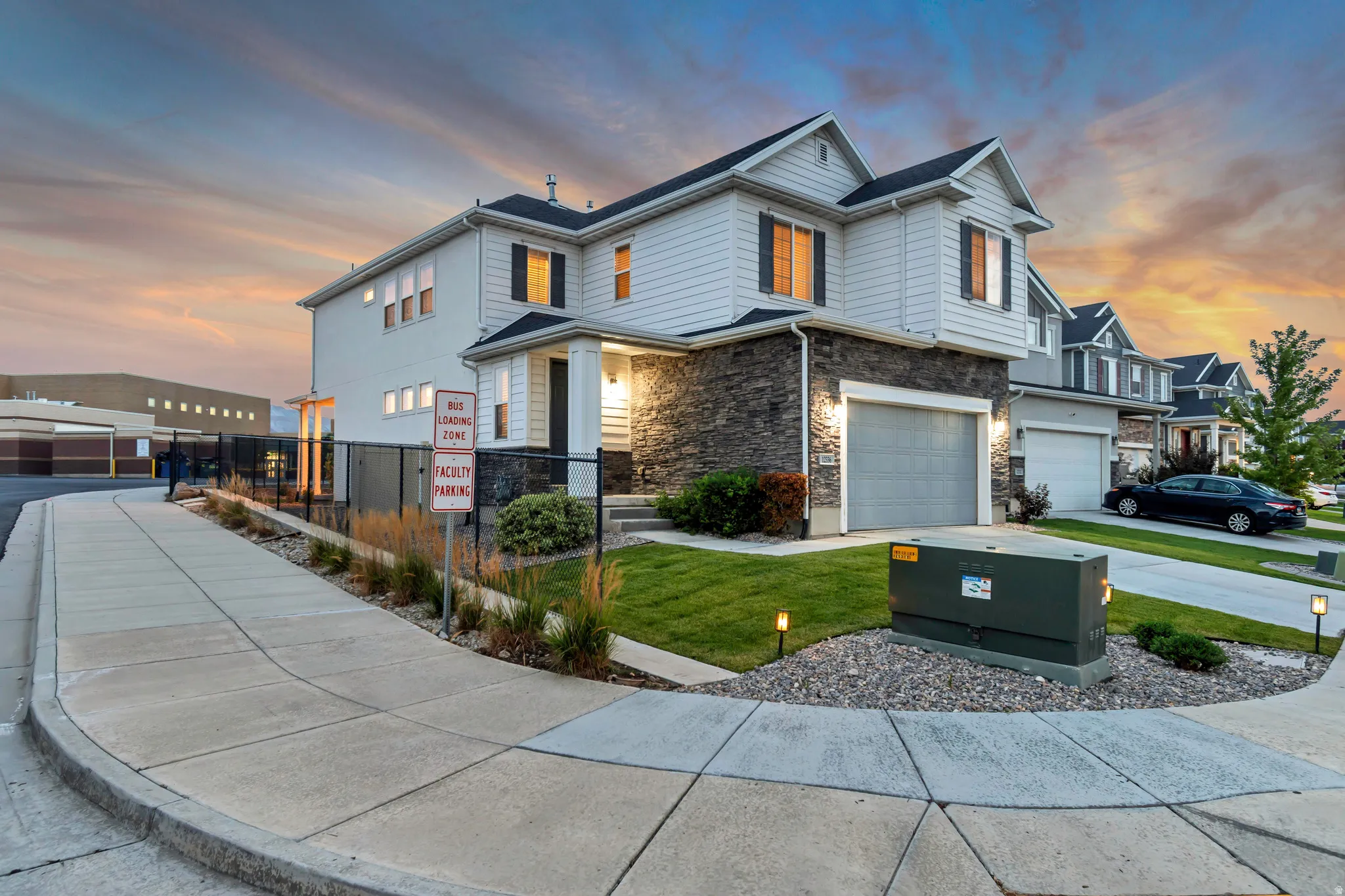 Two-story residence featuring light-colored siding, dark stone veneer, and a two-car garage