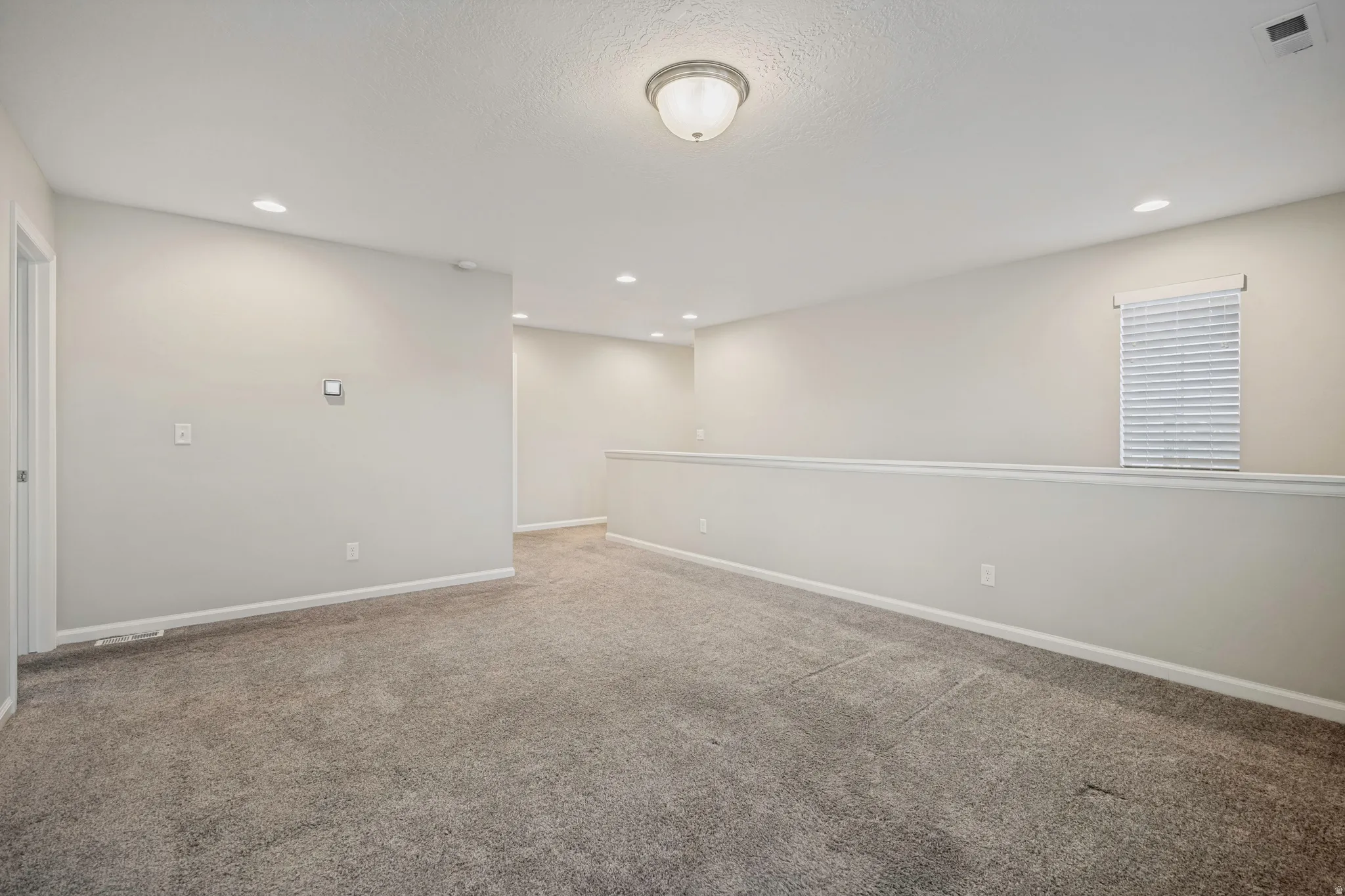 Expansive carpeted area featuring recessed lighting, a window with blinds, and an overhead flush-mount light fixture
