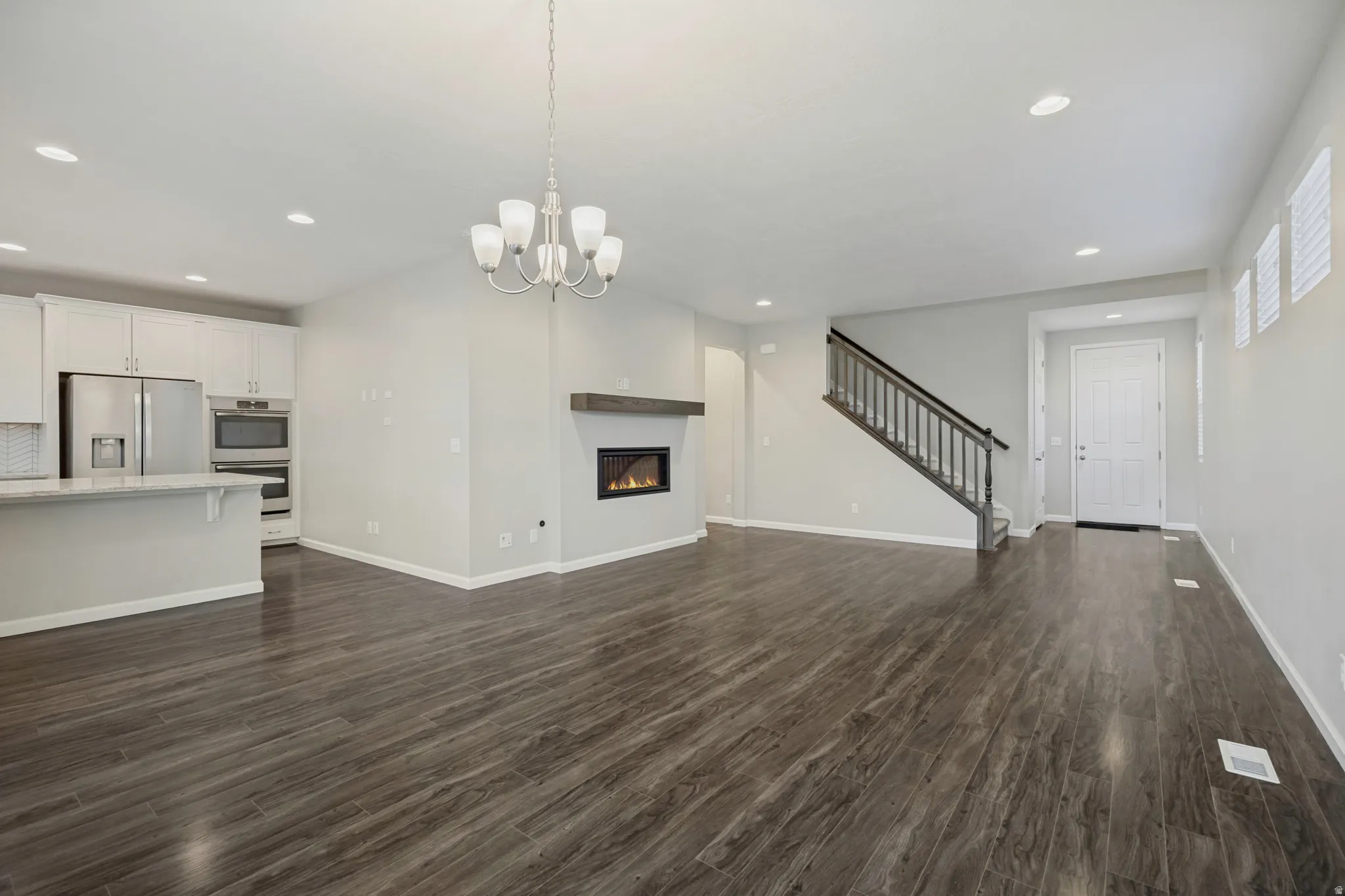 Open-concept living area with wood-finish flooring, a contemporary fireplace, and a kitchen featuring stainless steel appliances and white cabinetry