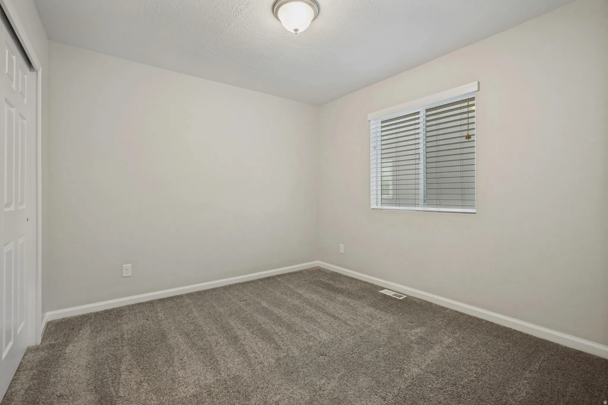 Carpeted flooring with light-toned walls, a window with blinds, and a flush mount ceiling light
