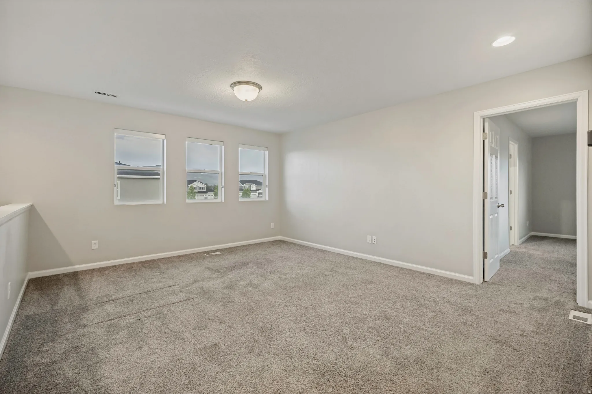 Spacious room featuring neutral carpet, light gray wall paint, three windows, and an overhead light fixture