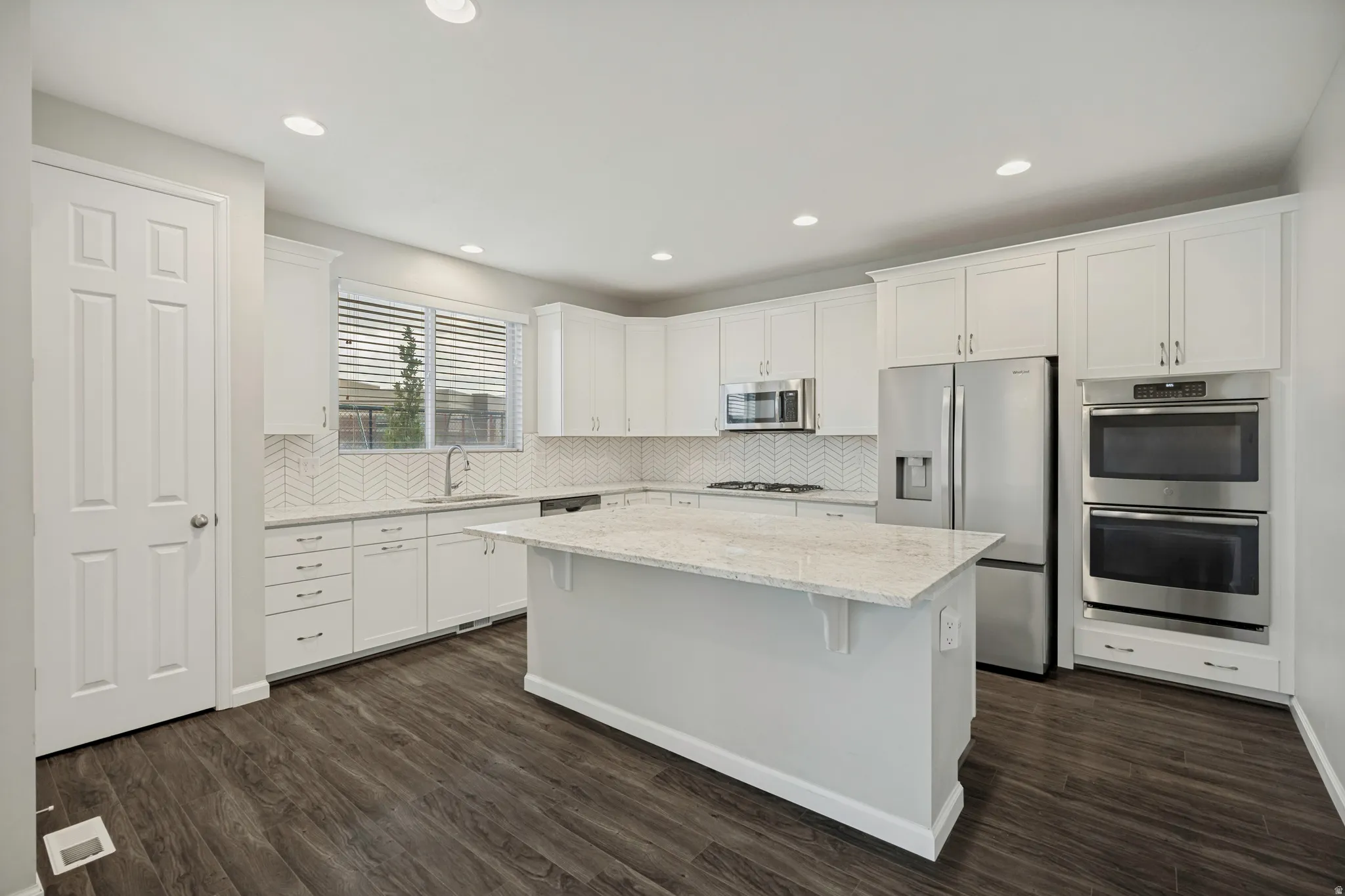 White cabinetry with stainless steel appliances, central island with stone countertop, dark wood-finish flooring, and recessed lighting