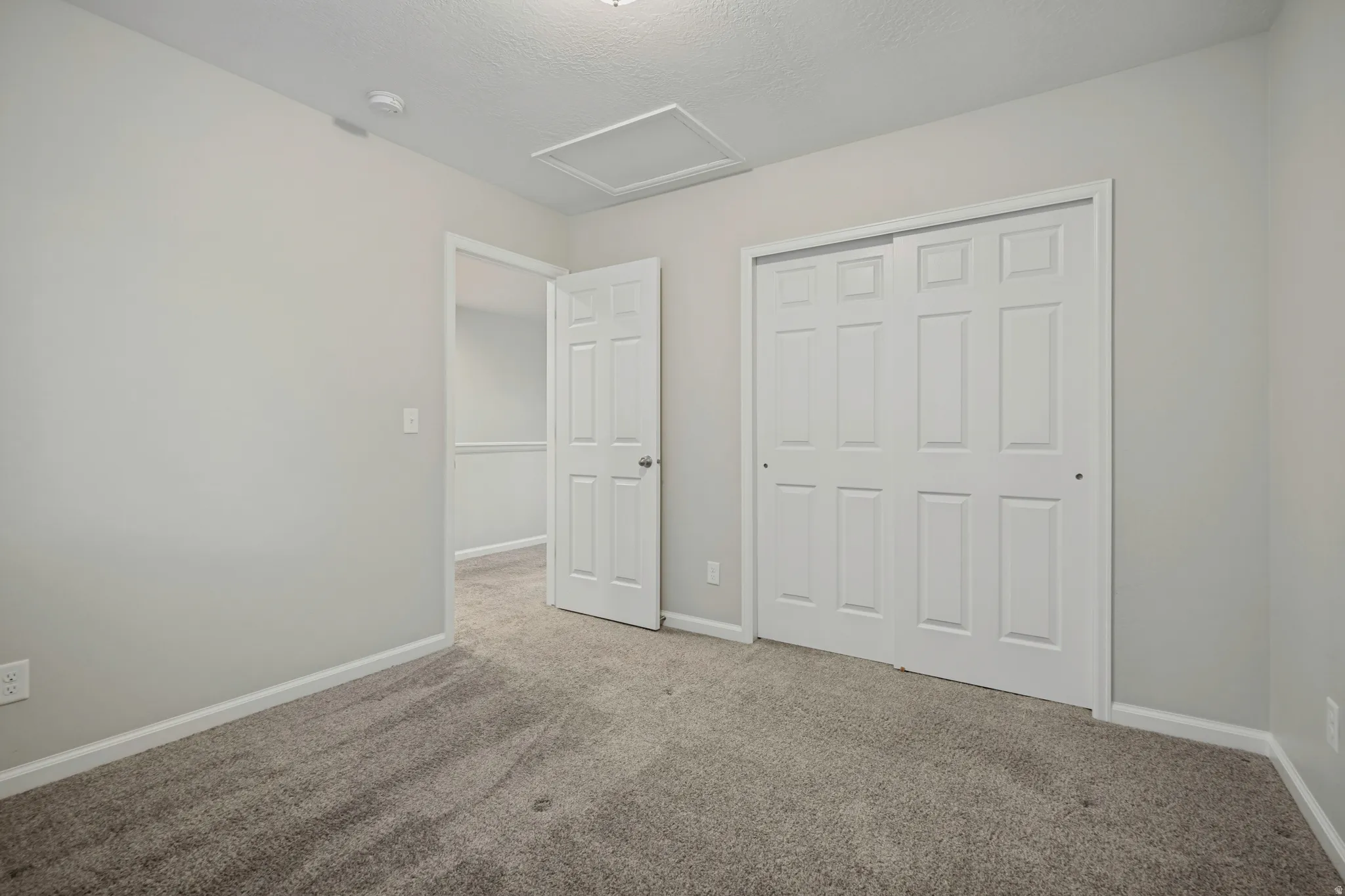 Neutral wall color, wall-to-wall carpeting, white bi-fold closet doors, white paneled door, and a ceiling-mounted light fixture