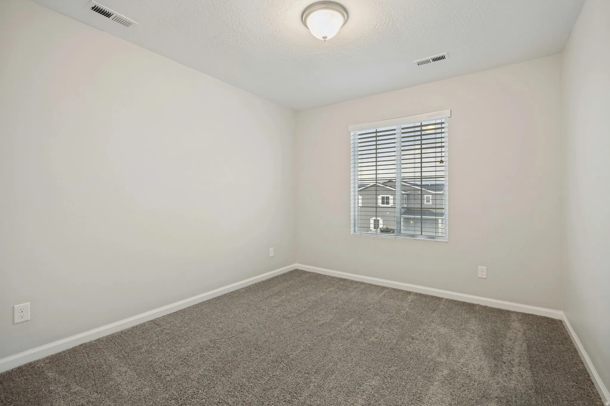 Neutral-toned walls, textured gray carpeting, and a window with blinds
