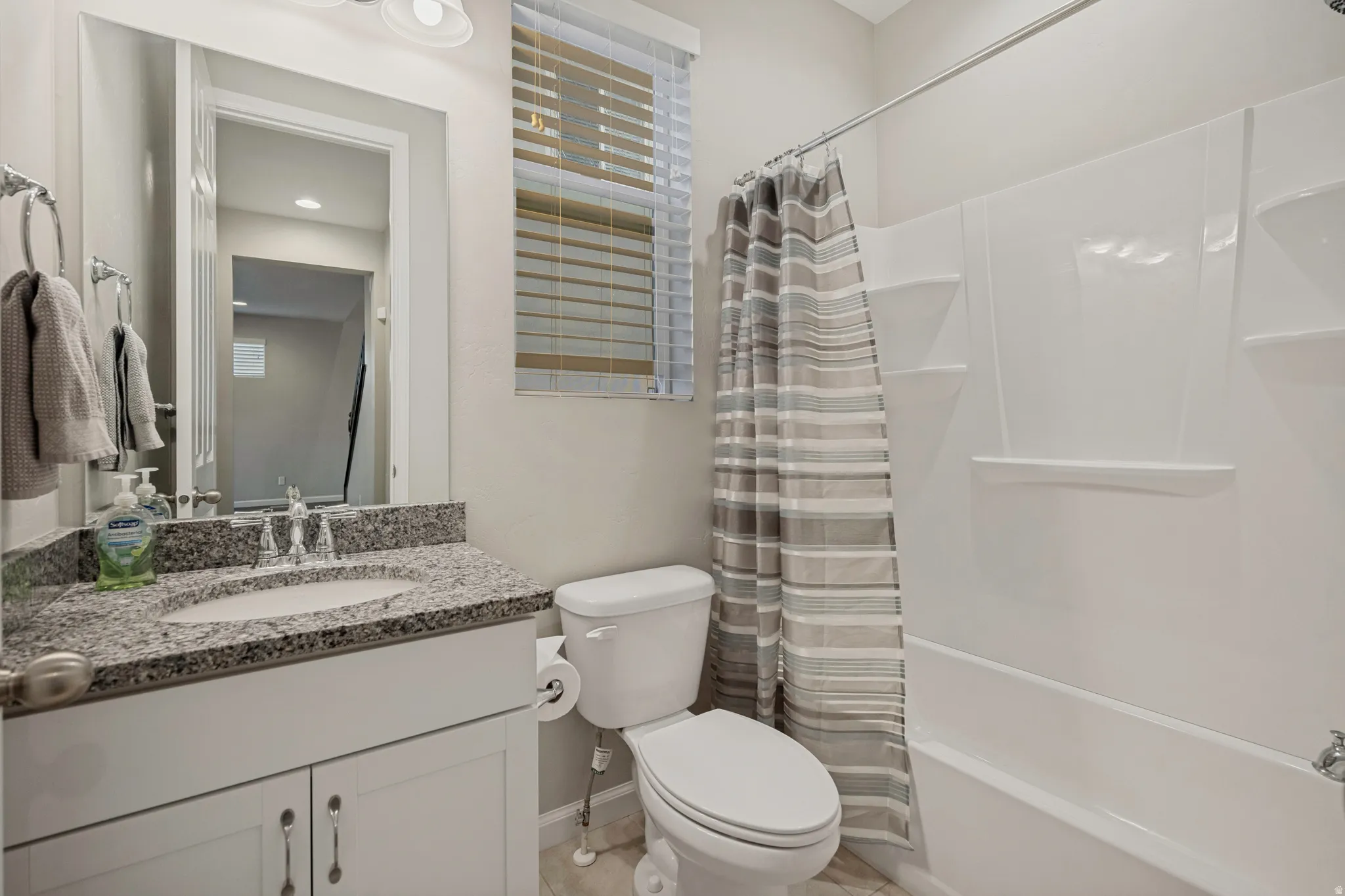 White vanity with granite countertop, integrated sink, chrome faucet, and mirrored wall cabinet