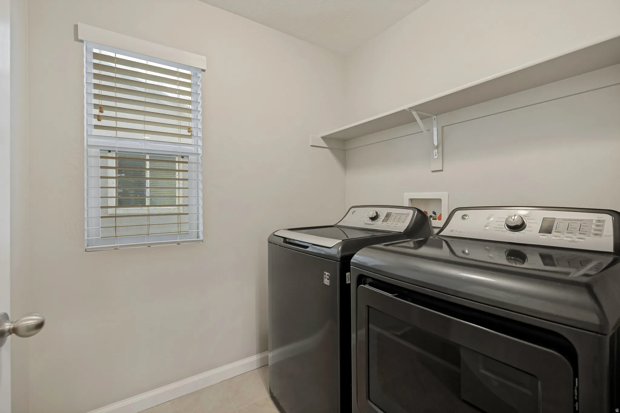 Laundry area featuring a window with blinds, upper storage shelving, and light-toned walls