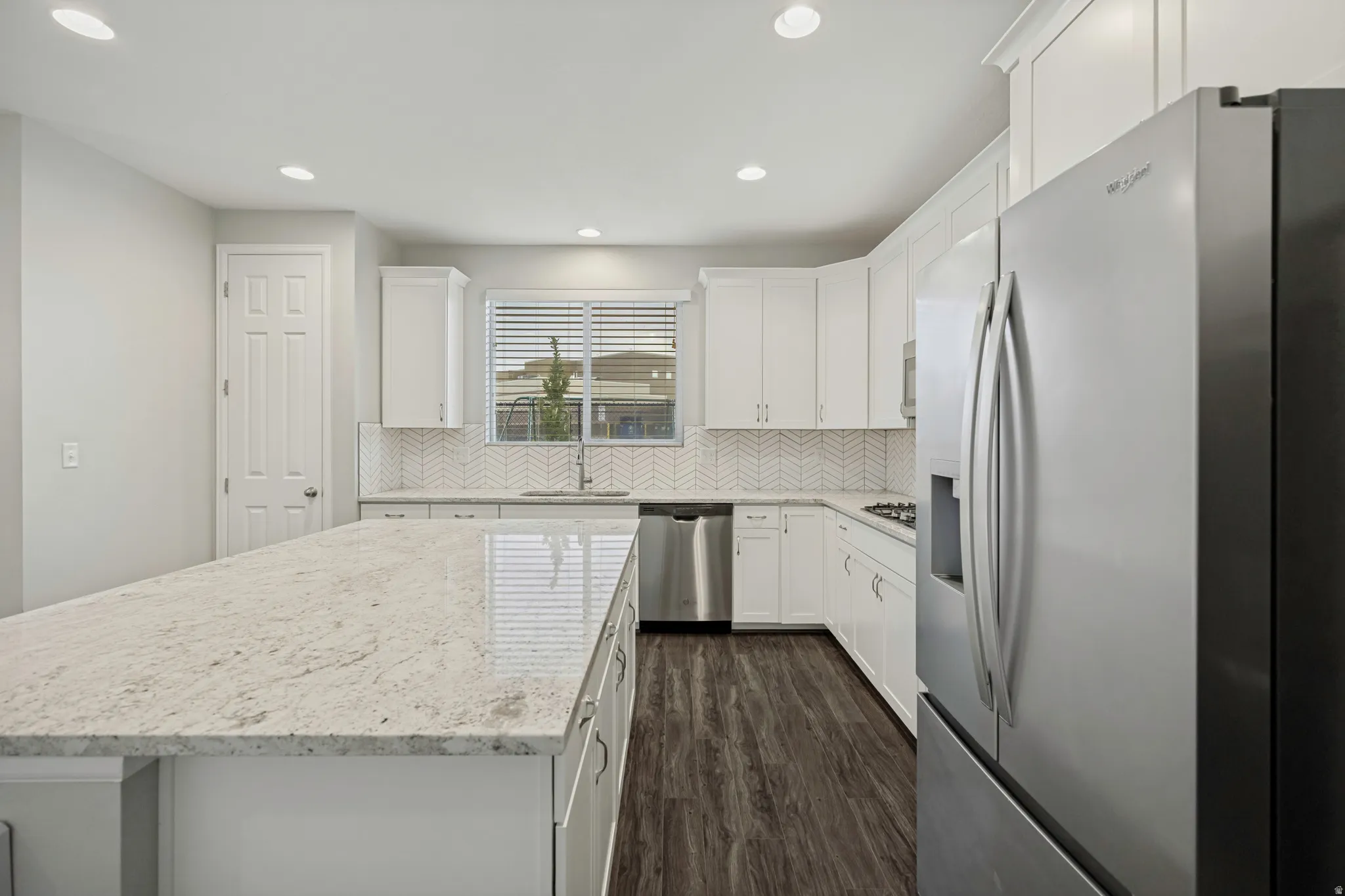 Spacious kitchen featuring a large island with a light-colored countertop, white cabinetry, stainless steel appliances, and wood-finish flooring