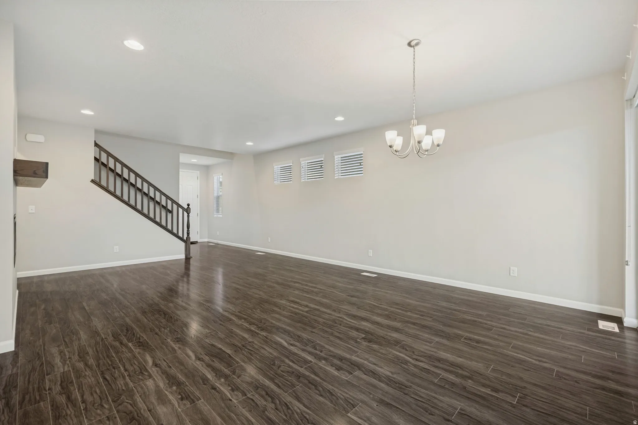 Spacious open-concept room featuring wood-finish flooring, recessed lighting, and a contemporary chandelier
