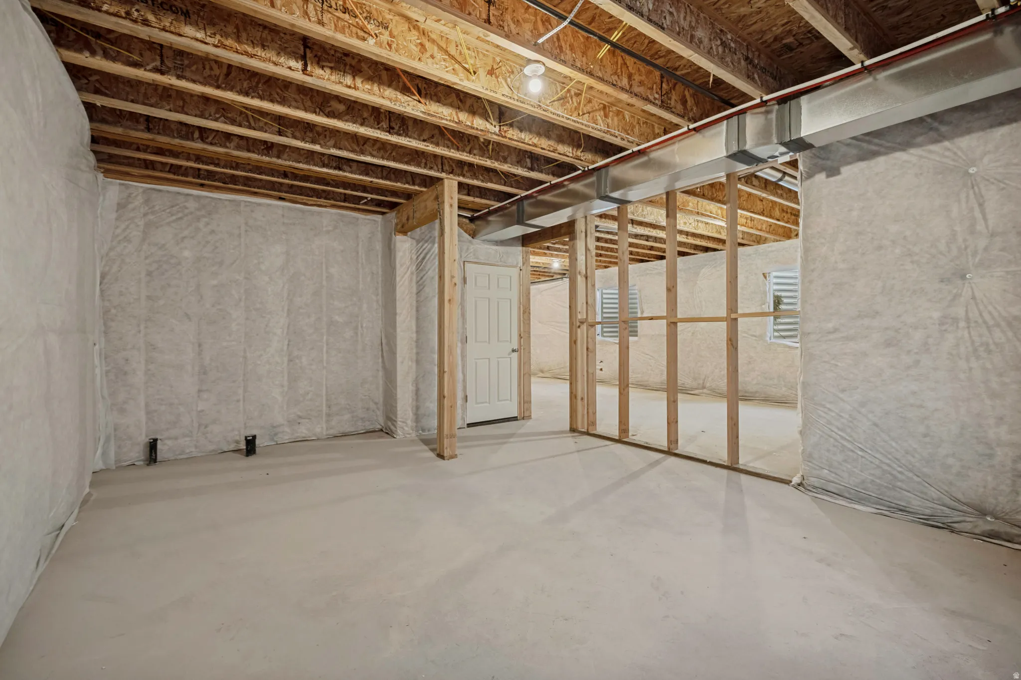 Unfinished basement with concrete flooring, exposed ceiling joists, framed walls, and visible ductwork