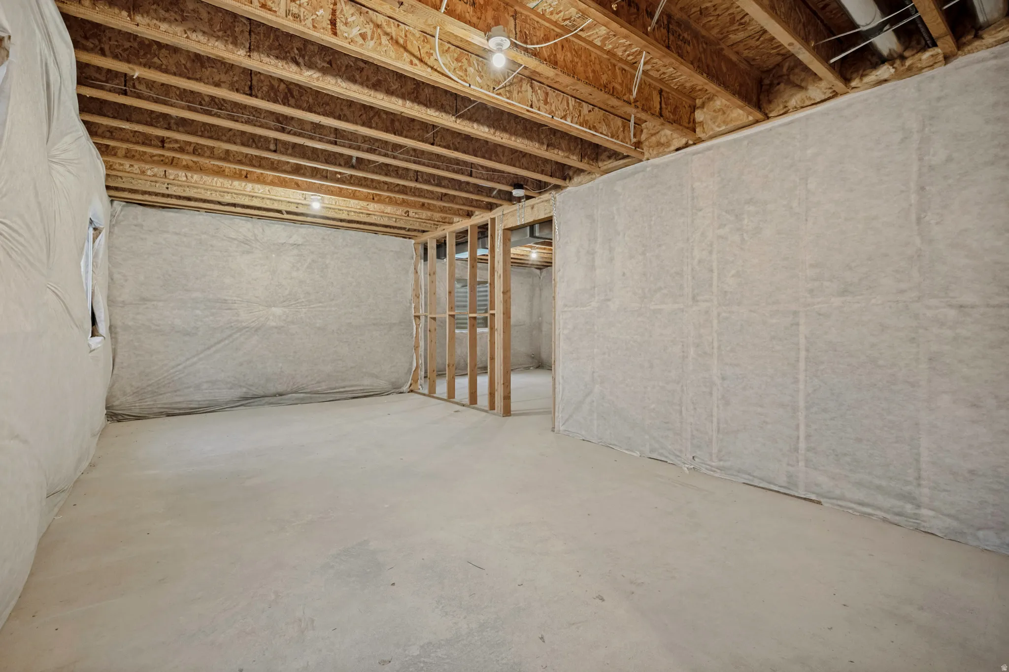 Unfinished basement with exposed ceiling joists, concrete flooring, and framed wall sections