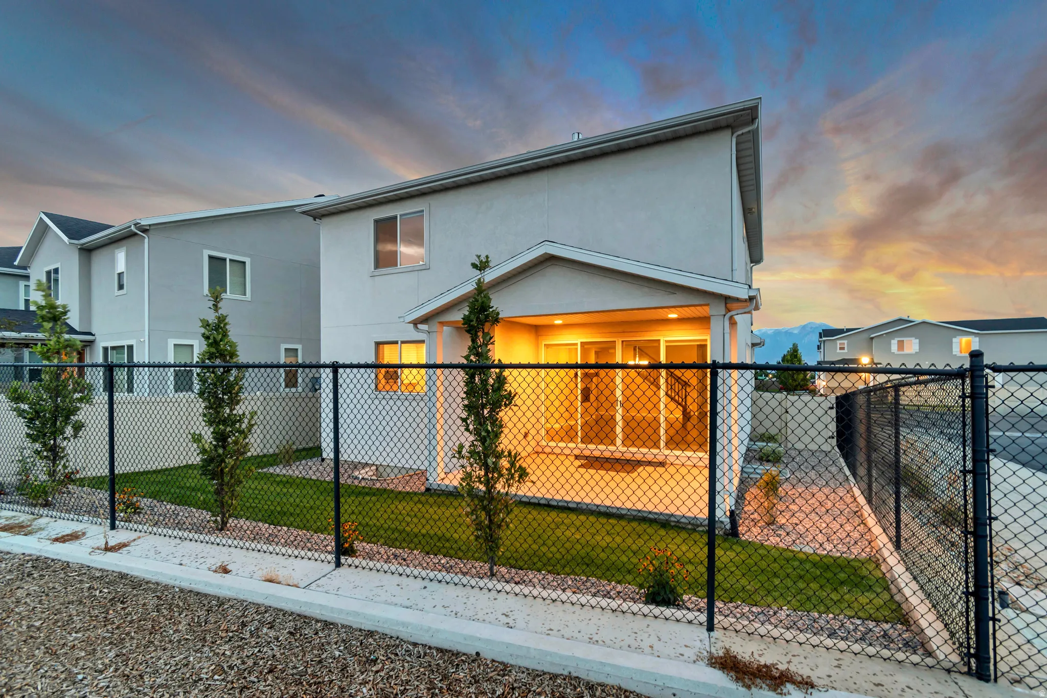 Rear exterior with stucco siding, covered patio, sliding glass doors, and a black chain-link fence