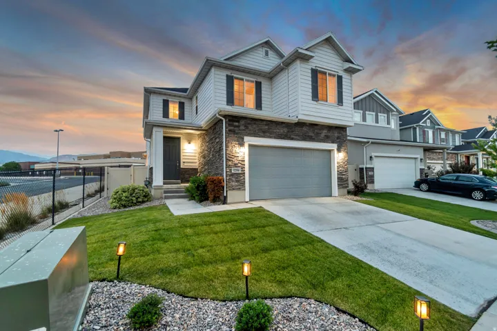 Two-story exterior with siding and stone accents, concrete driveway, attached garage, front yard with manicured lawn, and landscape lighting
