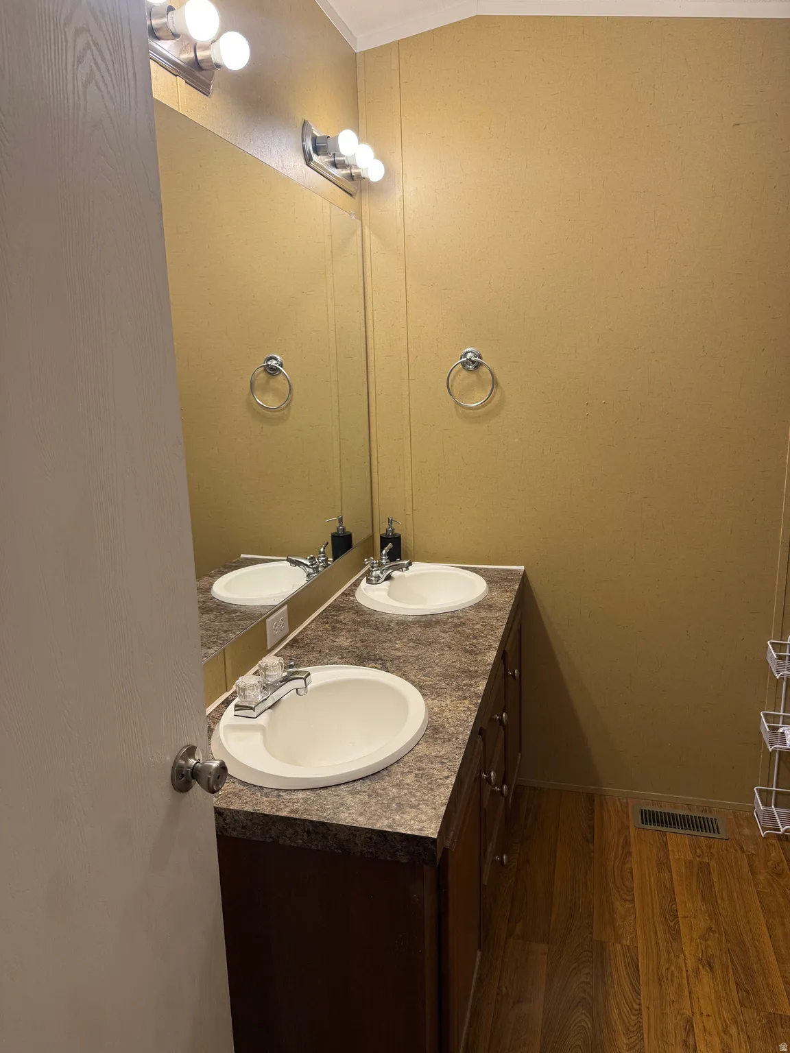 Dual vanity with integrated sinks, wood-finish flooring, full-width mirror, and overhead vanity lighting