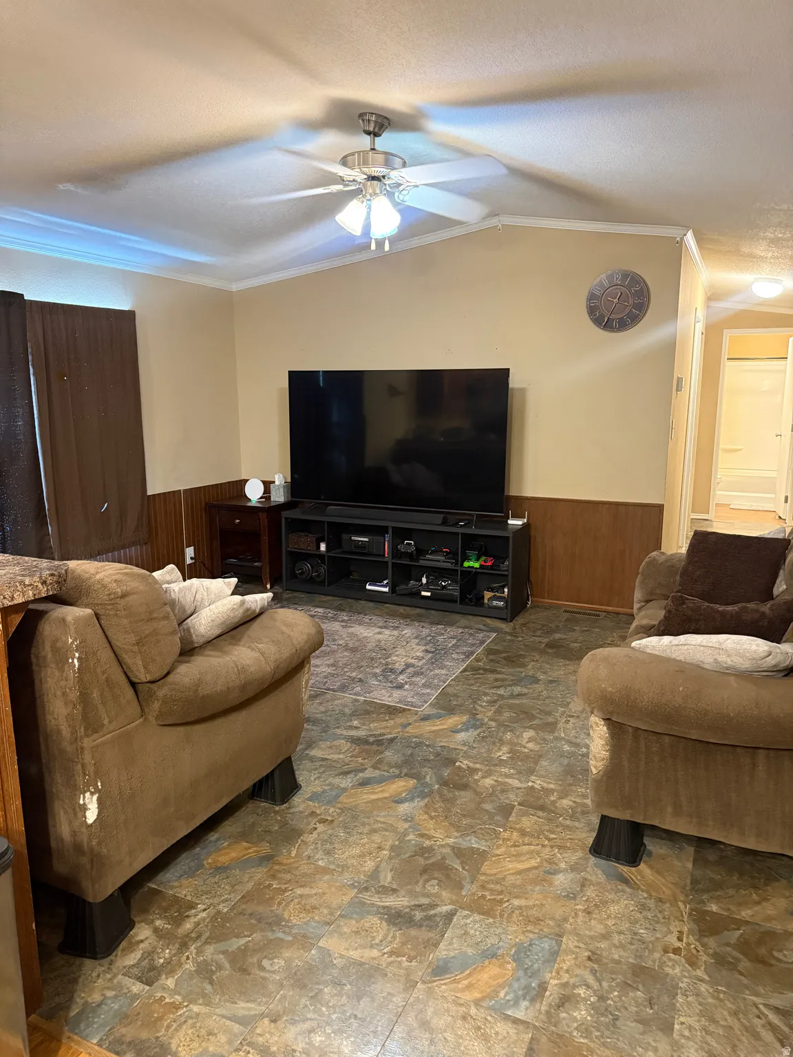 Spacious living room featuring neutral wall finishes, engineered wood-finish flooring, a ceiling fan with integrated lighting, and a black media console with open shelving