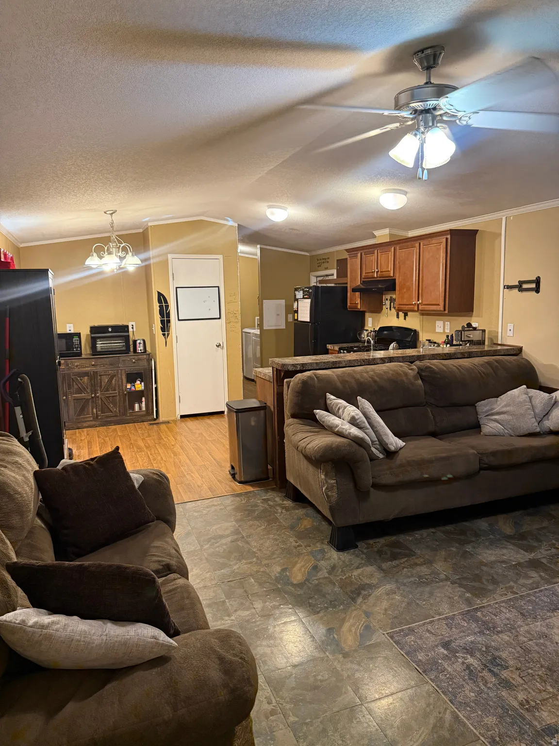 Open-concept living area featuring a ceiling fan with integrated lighting, wood-finish flooring, and a kitchen with wood cabinetry and a breakfast bar