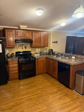 Kitchen featuring wood-finish flooring, ample cabinetry, L-shaped countertops, a gas range, and a built-in dishwasher