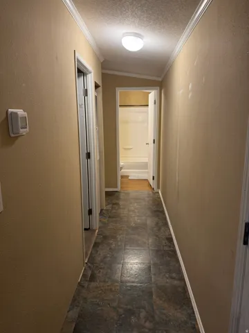 Hallway featuring tile-look flooring, crown molding, and a flush-mount ceiling light