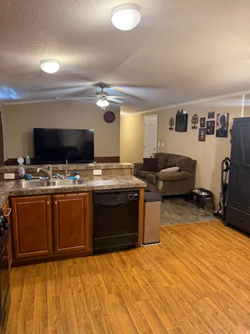 Kitchen featuring wood-finish flooring, a double basin stainless steel sink, black dishwasher, and wood-finish cabinetry
