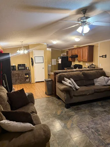 Open-concept living area featuring a ceiling fan with integrated lighting, wood-finish flooring, and a kitchen with wood cabinetry and a breakfast bar
