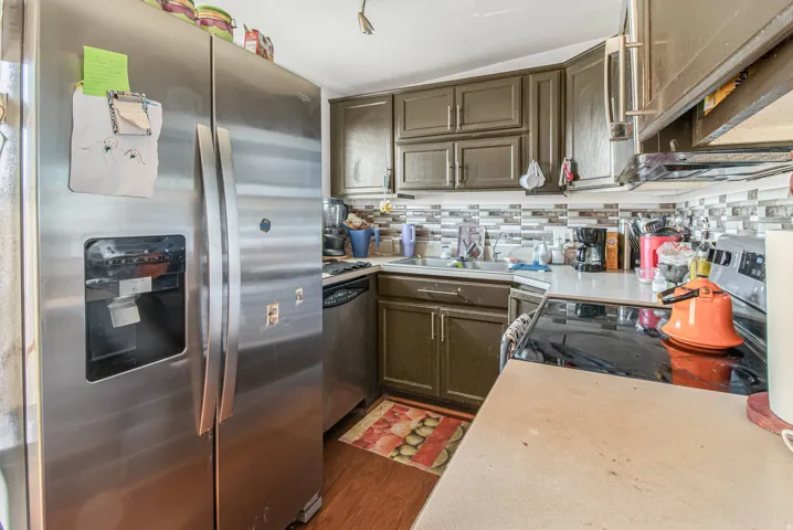 Kitchen featuring wood-finish flooring, stainless steel appliances, dark wood cabinetry, light countertops, and a mosaic tile backsplash