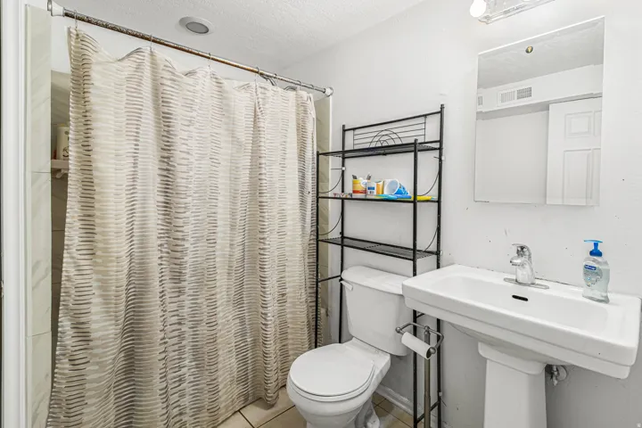 Pedestal sink with chrome faucet, wall-mounted mirror, and tile flooring