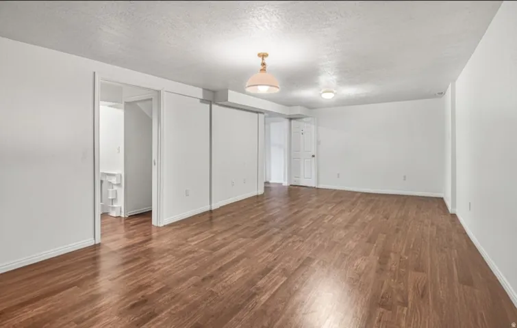 Spacious room featuring wood-finish flooring, white walls, and overhead lighting