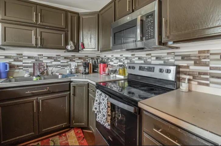 Kitchen featuring dark cabinetry, stainless steel microwave, stainless steel range, dual basin sink, and mosaic tile backsplash
