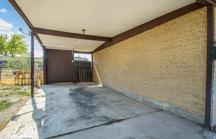 Covered carport featuring a concrete pad, textured block wall, and brown wood-finish beams