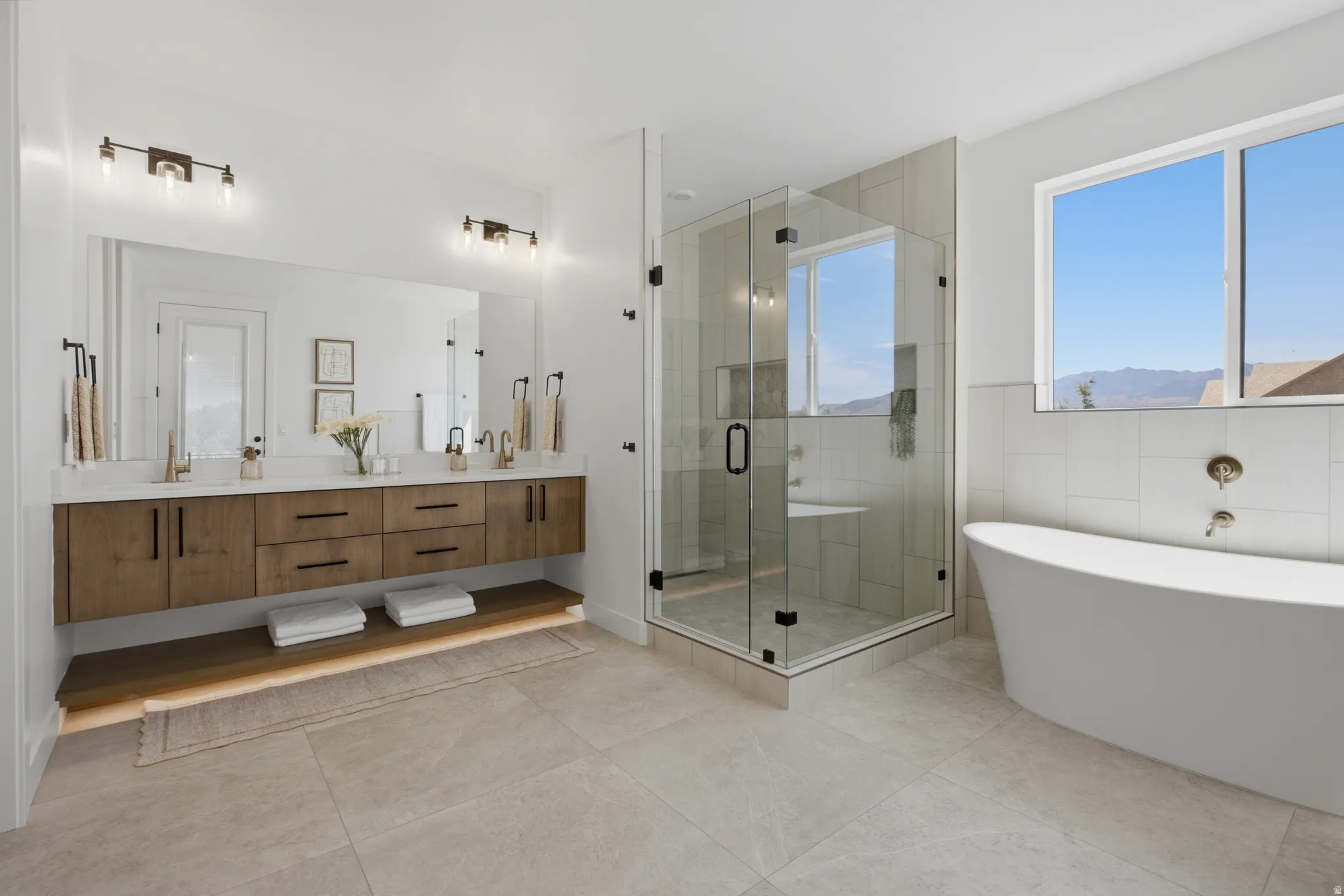 Floating dual vanity with wood-finish cabinetry, a large frameless mirror, and modern light fixtures