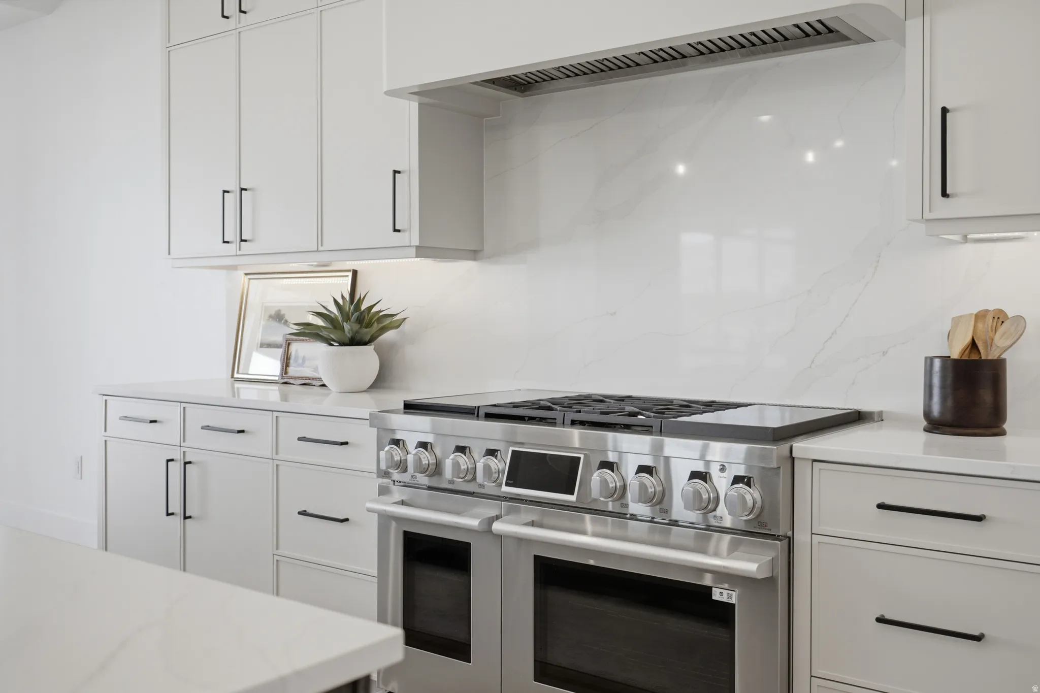 Stainless steel range with a built-in hood, quartz countertops, white cabinetry with black hardware, and a matching full-height backsplash