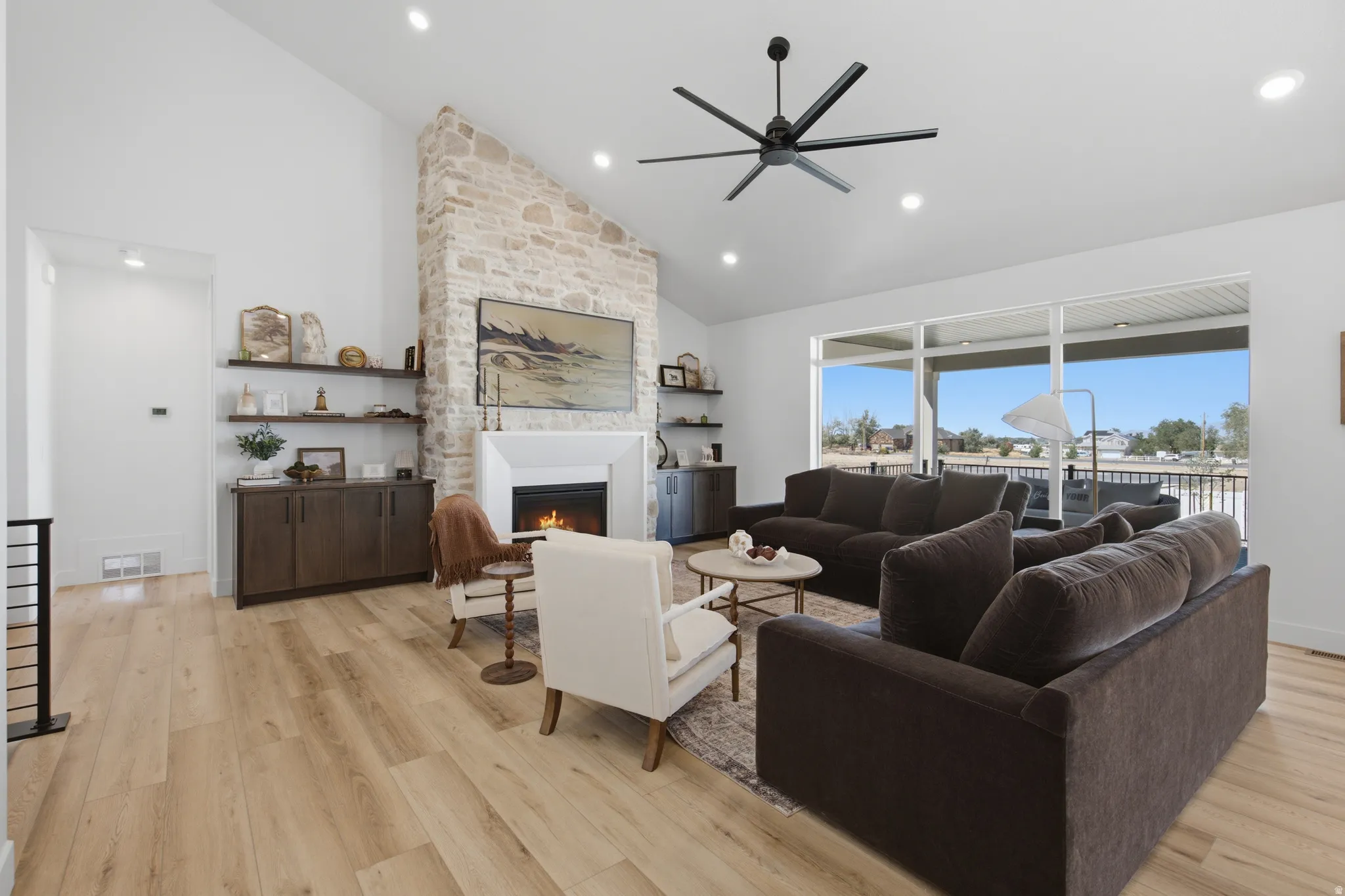 Vaulted ceiling with recessed lighting, stone-clad fireplace with mantel, built-in shelving, wood-finish flooring, and expansive sliding glass doors