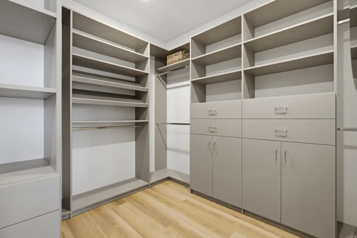 Custom closet system featuring built-in shelving, integrated drawers, cabinets with brushed nickel hardware, and wood-finish flooring